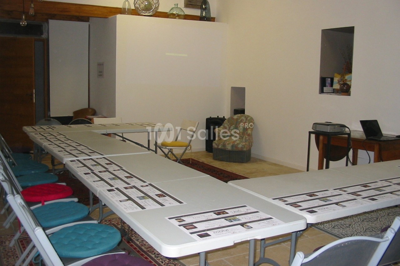 Salle de réunion avec des tables disposées en U, des chaises colorées et des documents alignés sur les tables.