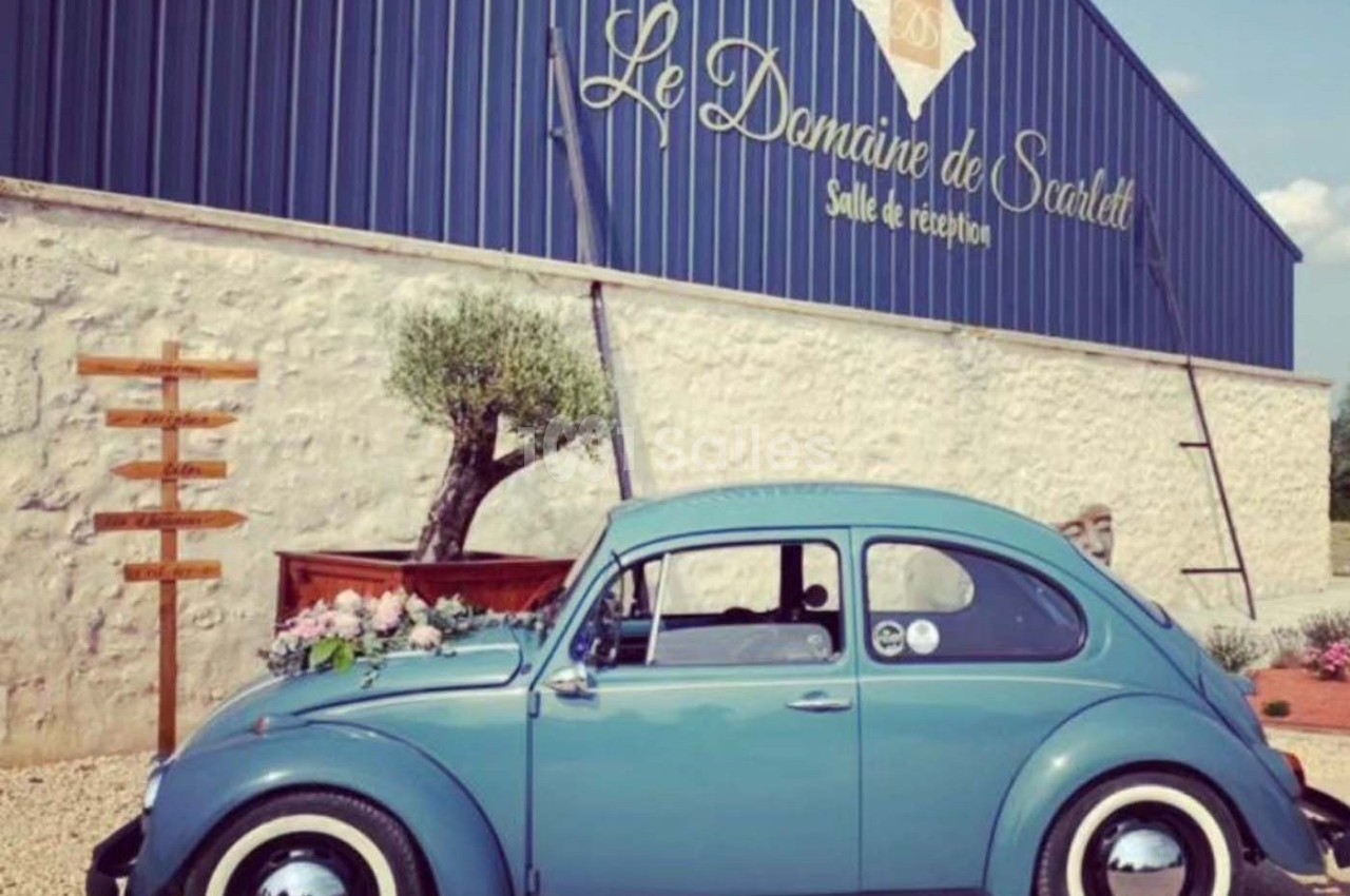 Voiture ancienne bleue garée devant un bâtiment en pierre avec une enseigne ’Le Domaine de Scarlett, Salle de réception’.