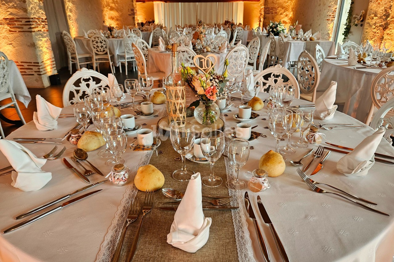 Salle de réception avec tables rondes élégamment dressées, nappes blanches, vaisselle raffinée et décoration florale.