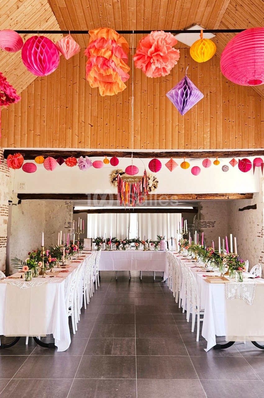 Salle de réception décorée avec des guirlandes colorées, des tables dressées et des compositions florales.