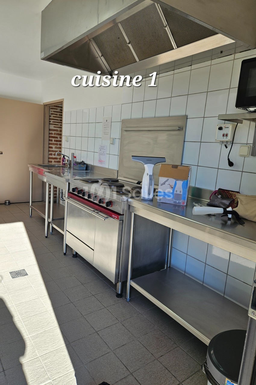 Cuisine professionnelle avec plaques de cuisson, hotte, plans de travail en inox et carrelage mural blanc.