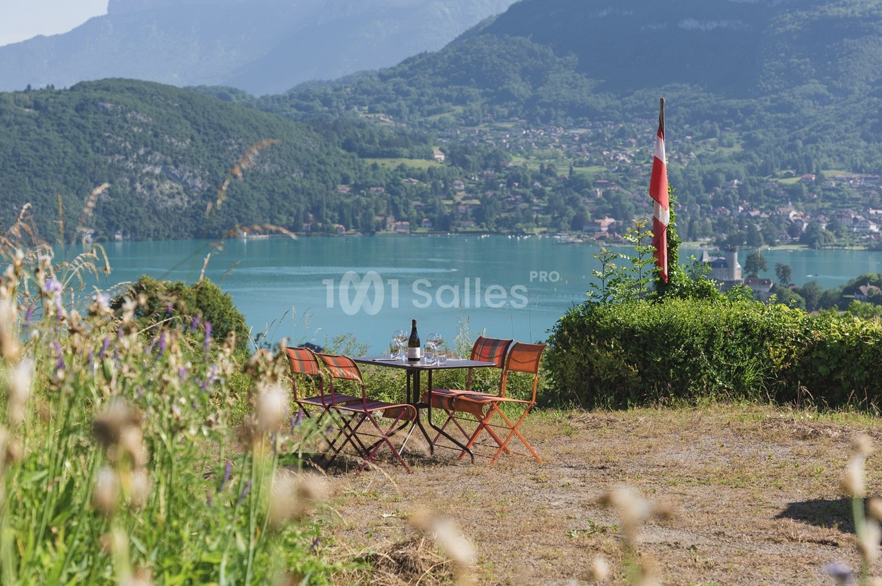 Table et chaises colorées sur une colline avec vue sur un lac, des montagnes et un drapeau en arrière-plan.