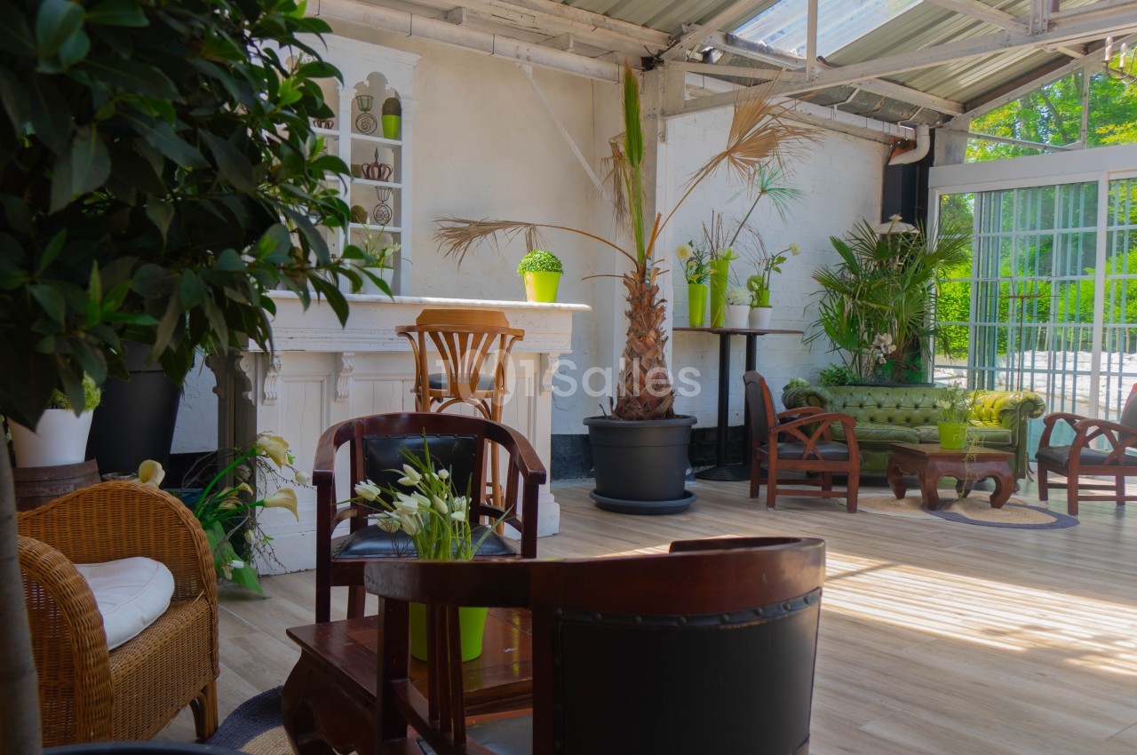 Espace lumineux avec mobilier en bois, plantes vertes et grandes baies vitrées donnant sur un extérieur verdoyant.