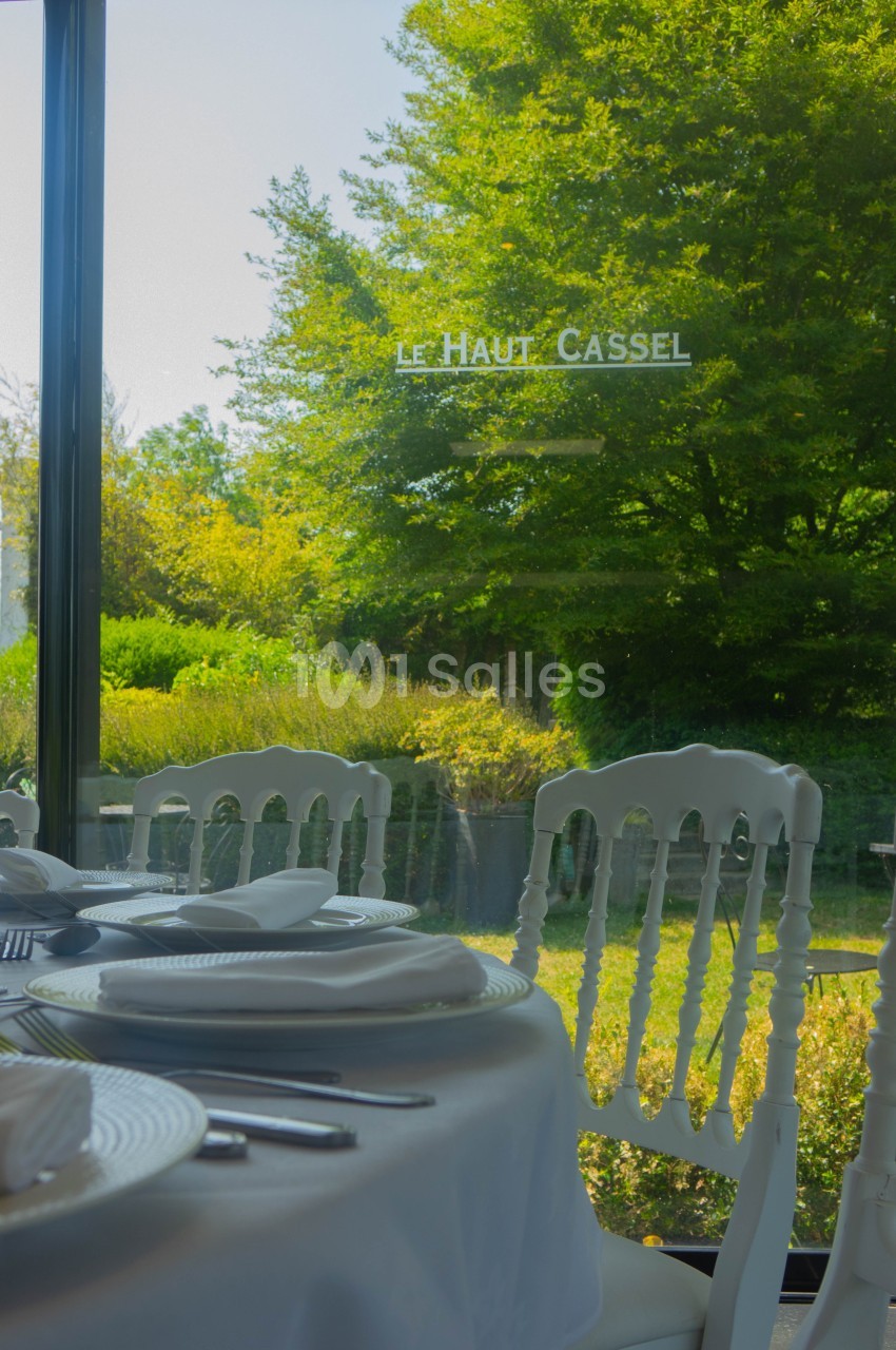 Salle de restaurant avec table dressée, vue sur un jardin verdoyant à travers une grande baie vitrée.