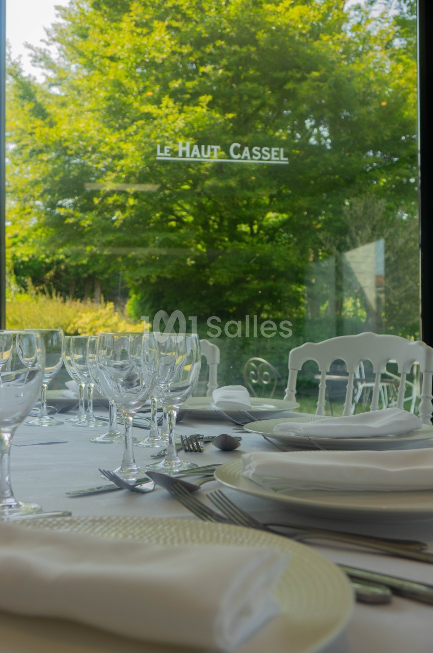 Table dressée avec vaisselle et verres élégants, vue sur un jardin verdoyant à travers une grande baie vitrée.