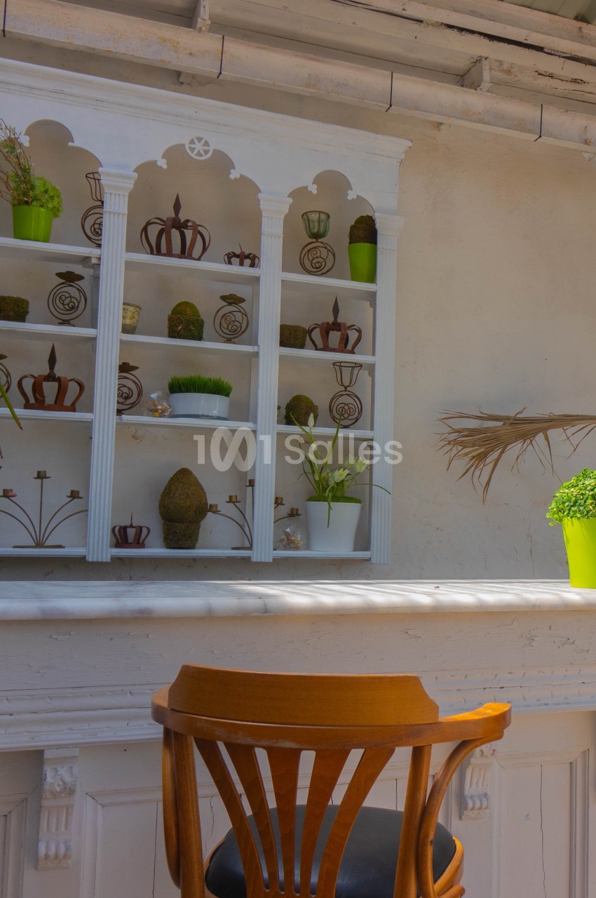 Étagère blanche décorative avec plantes et objets, devant un mur clair, une chaise en bois au premier plan.
