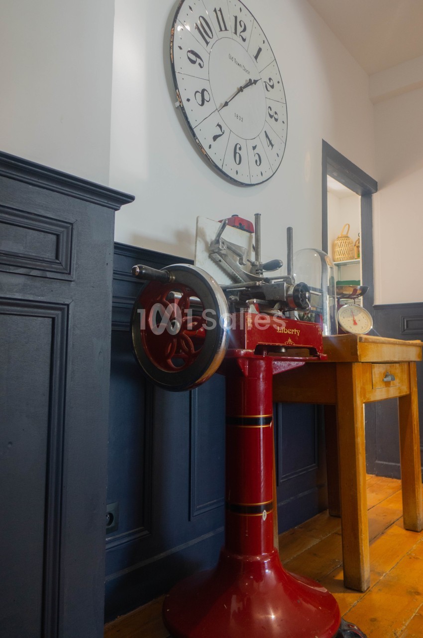 Machine à trancher rouge vintage posée près d'une table en bois, avec une grande horloge murale en arrière-plan.