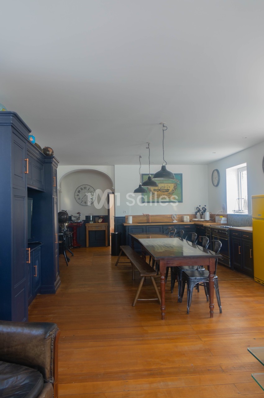 Cuisine spacieuse avec meubles bleu foncé, table en bois, chaises métalliques, réfrigérateur jaune et horloge murale.