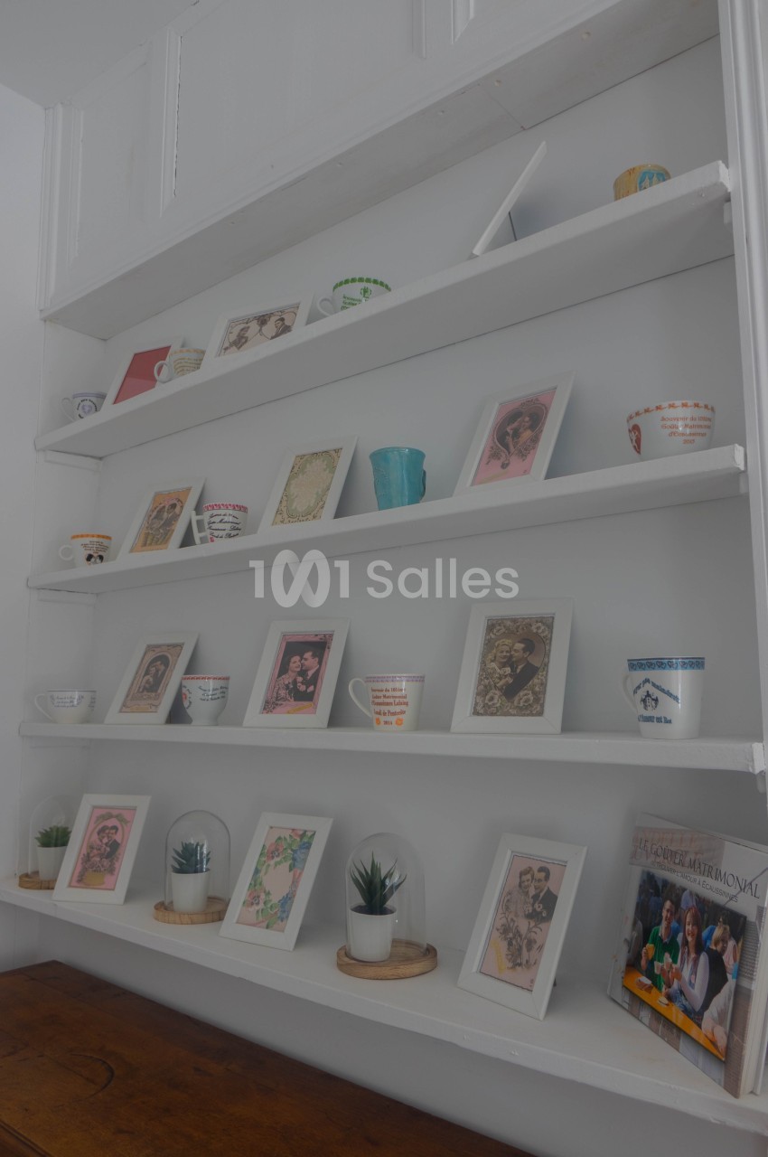 Étagères blanches décorées de cadres, tasses colorées, plantes et magazines sur un meuble en bois.