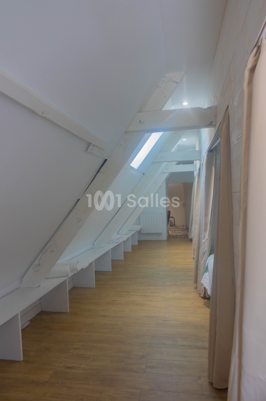 Couloir mansardé avec poutres apparentes blanches, parquet clair et rideaux séparant des espaces.
