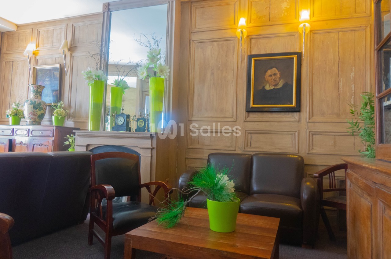 Salon avec fauteuils en cuir, table basse, plantes vertes en pots et portrait encadré sur un mur en bois clair.