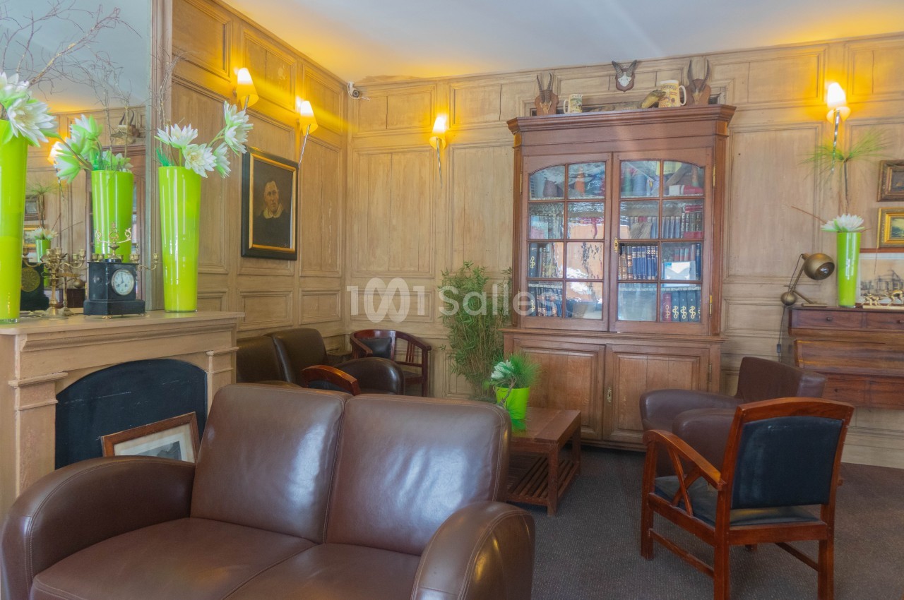 Salon chaleureux avec fauteuils en cuir, bibliothèque en bois, cheminée et décorations florales vertes.