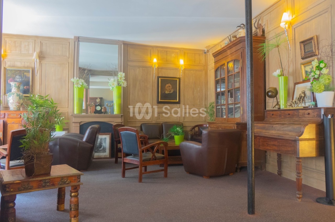 Salon chaleureux avec fauteuils en cuir, table basse en bois, bibliothèque vitrée et décoration végétale.