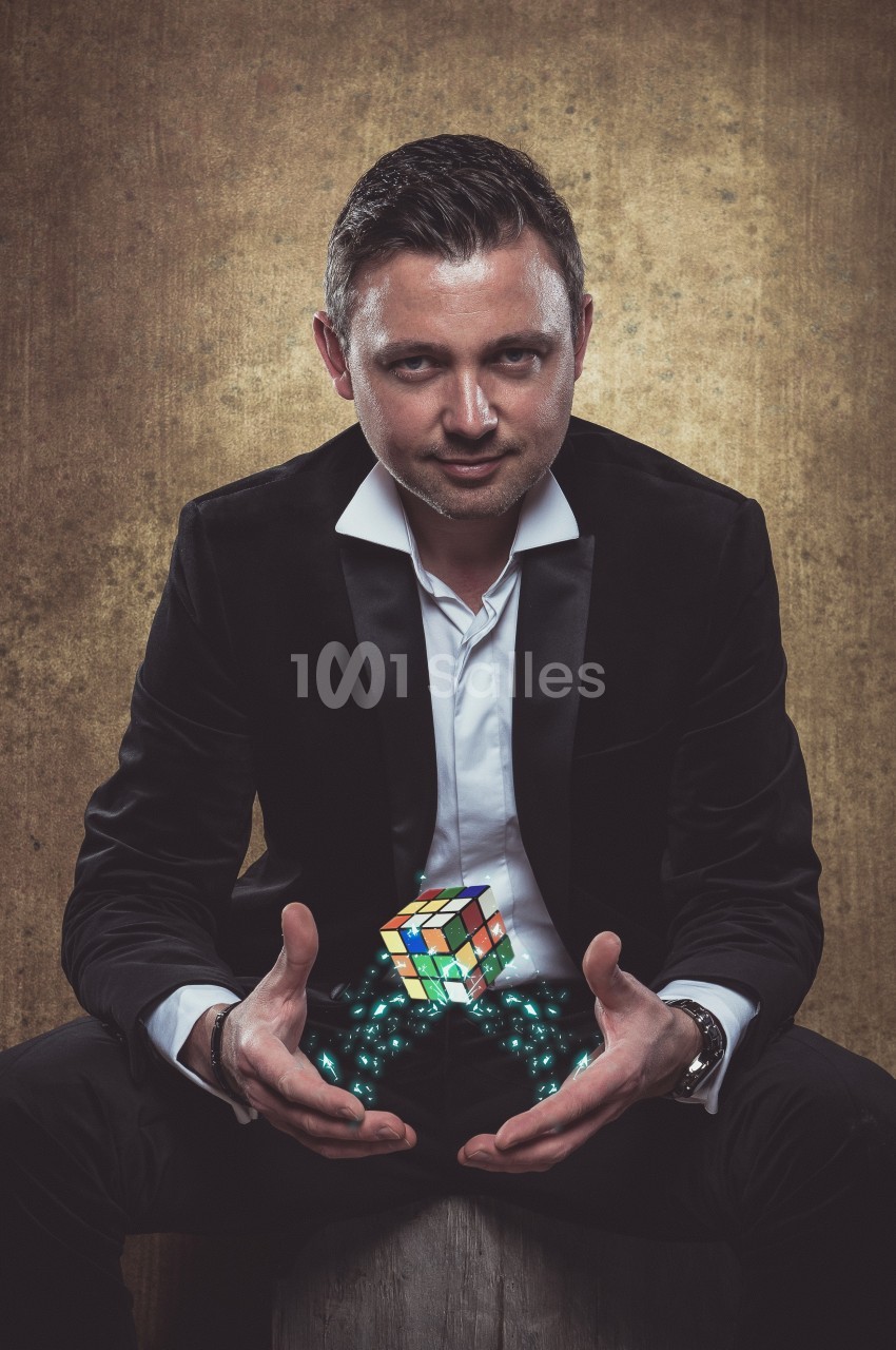 Un homme en costume noir tient un Rubik's Cube lumineux entre ses mains devant un fond texturé.