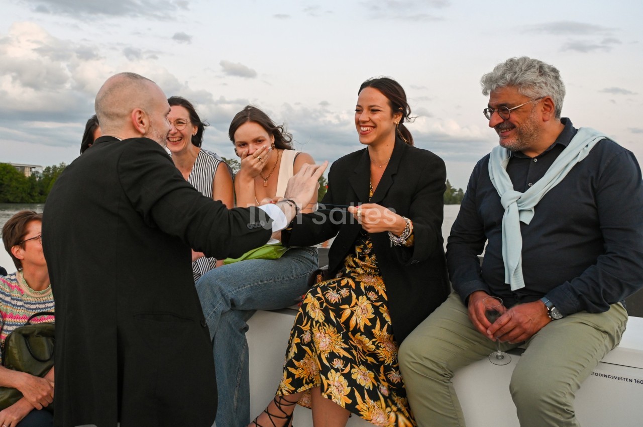 Un groupe de personnes assises à l'extérieur, souriant et échangeant lors d'un moment convivial en fin de journée.
