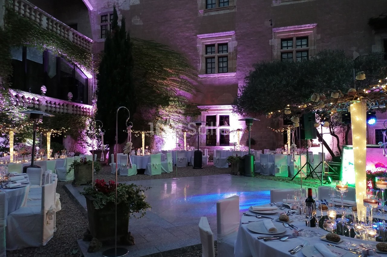 Cour intérieure éclairée pour un dîner en plein air, avec tables dressées, décorations lumineuses et ambiance festive.