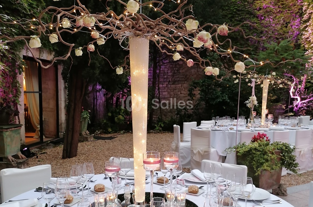 Table de réception élégamment décorée avec des guirlandes lumineuses, des roses suspendues et des assiettes dressées en…