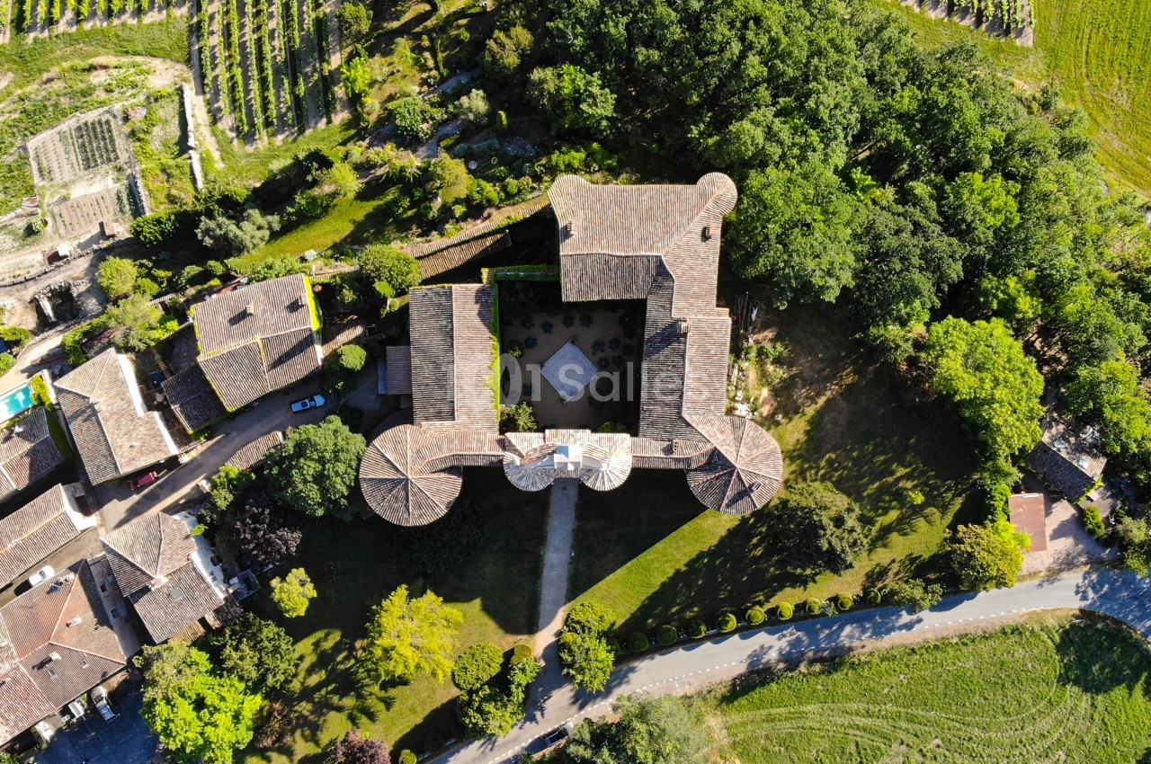 Vue aérienne d'un bâtiment historique entouré de jardins, de vignes et de maisons dans un paysage rural.