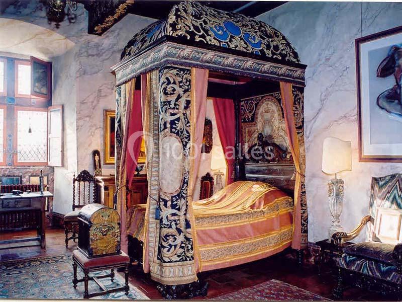 Lit à baldaquin richement décoré dans une chambre ancienne avec meubles en bois sculpté et tentures colorées.
