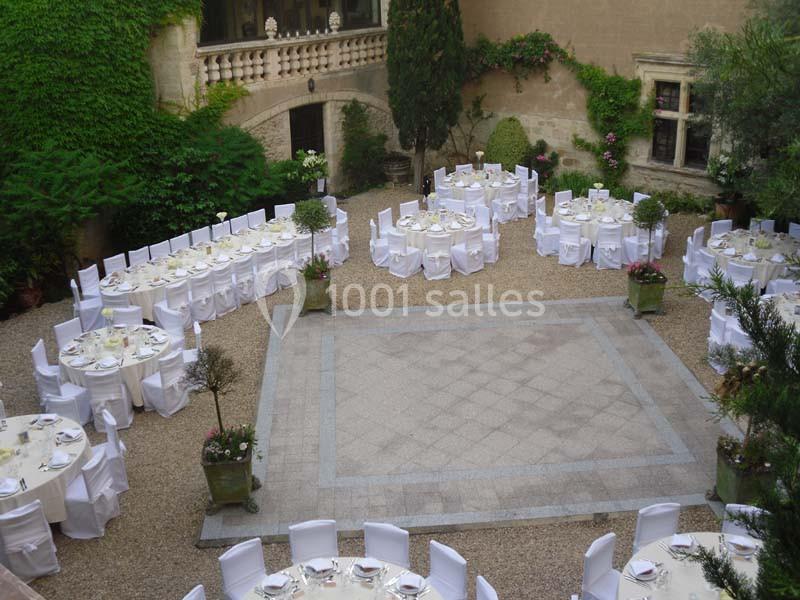 Cour intérieure aménagée pour un événement avec des tables rondes dressées et des chaises blanches, entourée de murs en…
