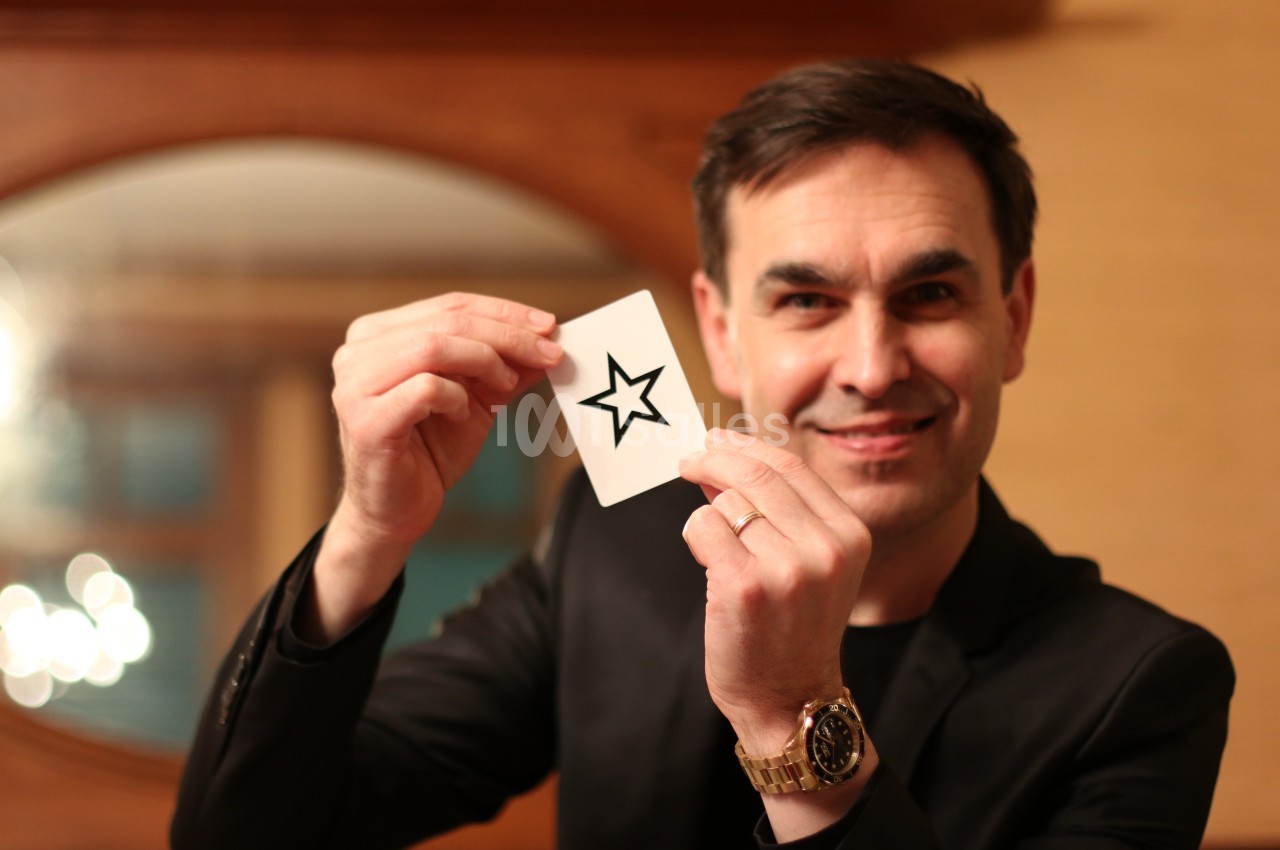 Un homme souriant tient une carte blanche avec une étoile noire imprimée, dans un intérieur chaleureux.