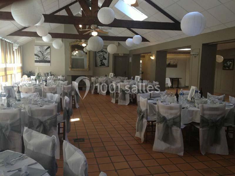 Salle de réception décorée avec des tables dressées, chaises couvertes de housses blanches et lanternes suspendues.
