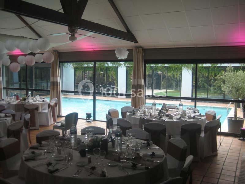 Salle de réception décorée avec tables dressées, donnant sur une piscine visible à travers de grandes baies vitrées.