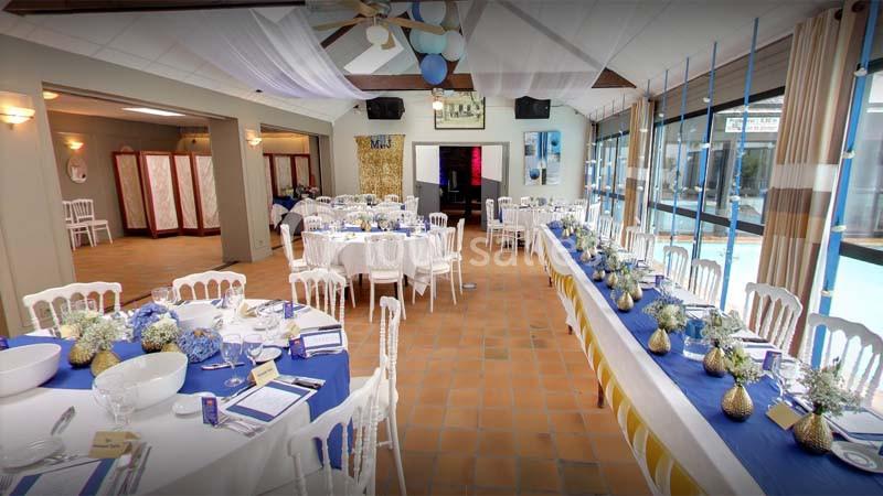 Salle de réception décorée avec des tables dressées, ornées de fleurs et de nappes blanches et bleues.