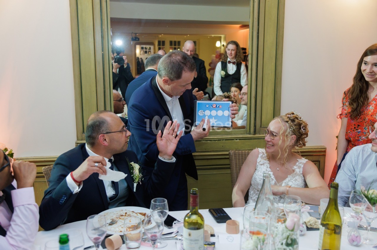 Un homme montre un dessin humoristique à des invités assis à une table lors d'une réception festive.