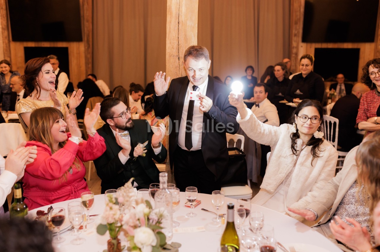 Un homme en costume réalise un tour de magie avec une lumière devant des invités assis autour d'une table lors d'un…