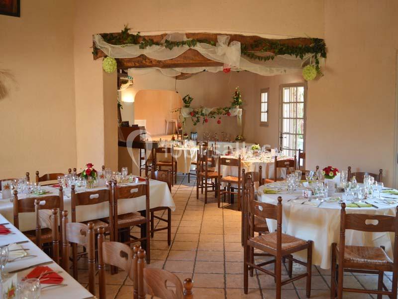 Salle de réception décorée avec des tables rondes dressées, chaises en bois et guirlandes suspendues.