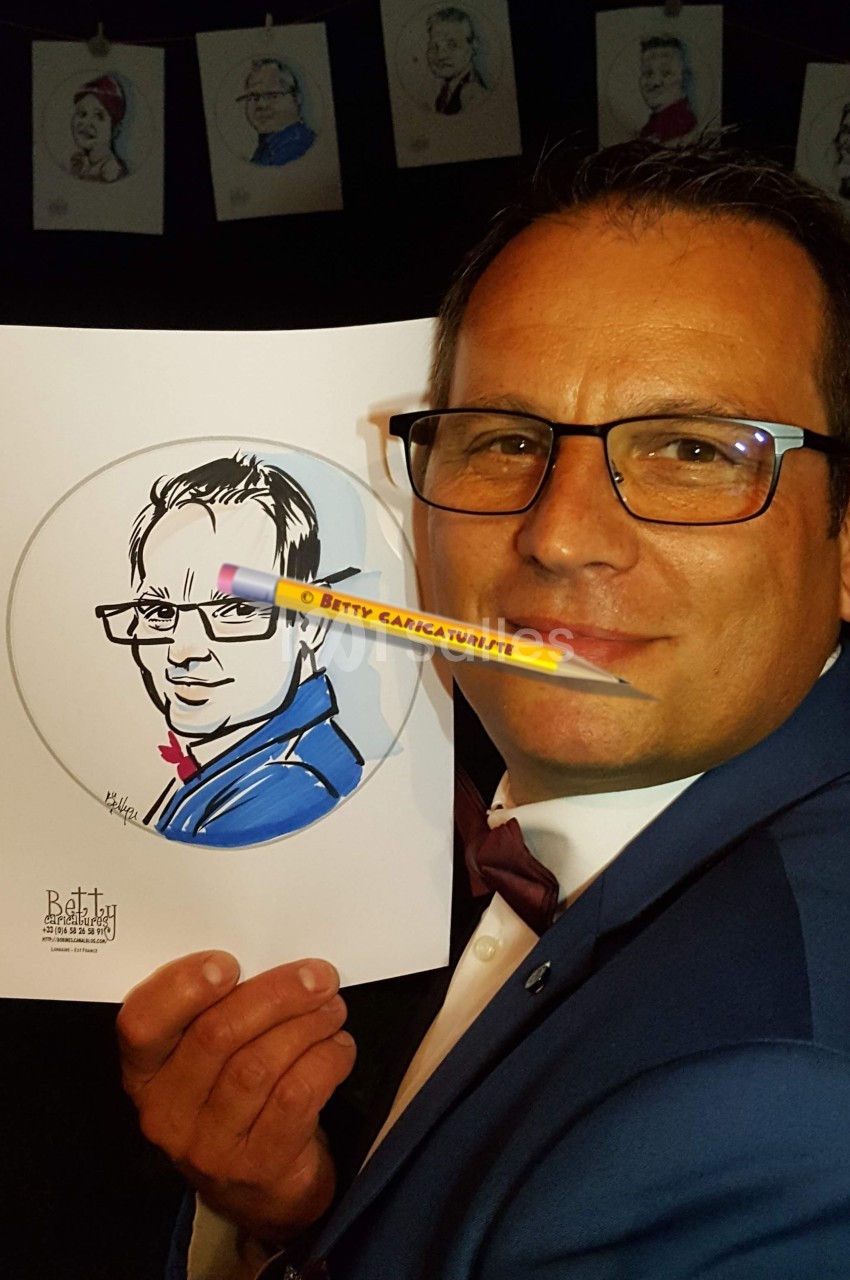 Homme en costume tenant un dessin caricatural de lui-même, avec des portraits accrochés en arrière-plan.