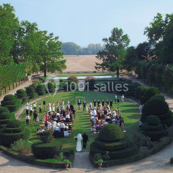 Cérémonie en plein air dans un jardin entouré de haies taillées, avec des invités assis en cercle.