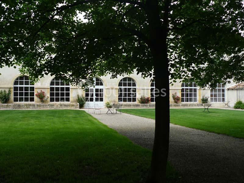 Façade d’un bâtiment avec de grandes fenêtres cintrées, entourée de pelouses et d’arbres dans un jardin.