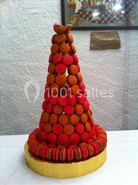 Croquembouche aux choux rouges et orangés disposés en pyramide sur socle jaune.