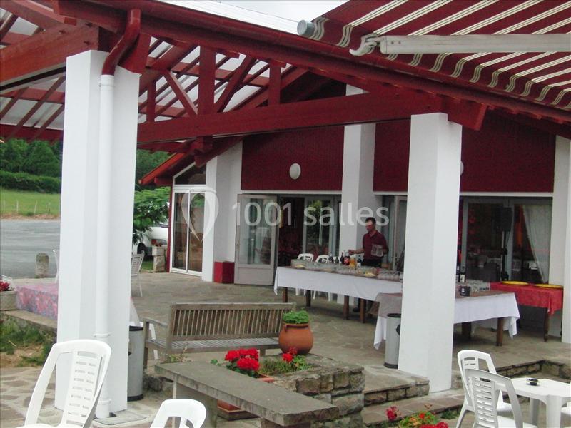 Terrasse couverte avec pergola rouge et blanc, colonnes blanches, chaises longues, banc en bois et fleurs rouges.