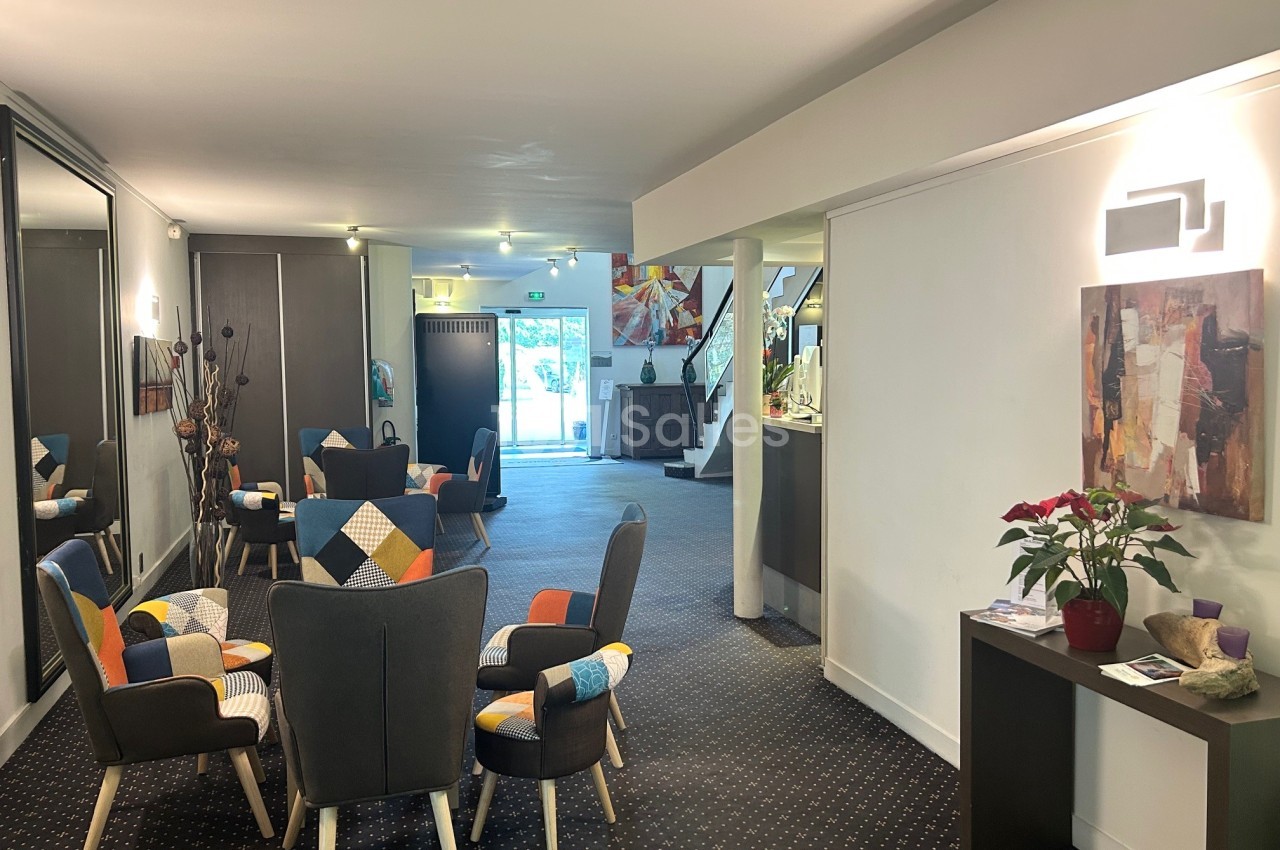 Espace d'accueil lumineux avec fauteuils colorés, table basse, miroir et comptoir près d'une entrée vitrée.