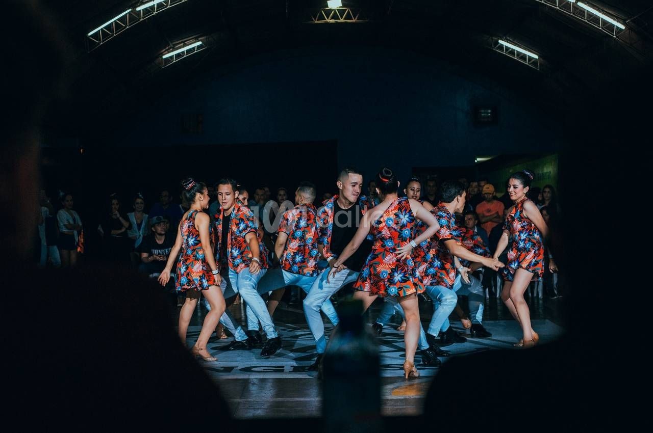 Un groupe de danseurs en tenue colorée exécute une chorégraphie sur une scène éclairée devant un public.