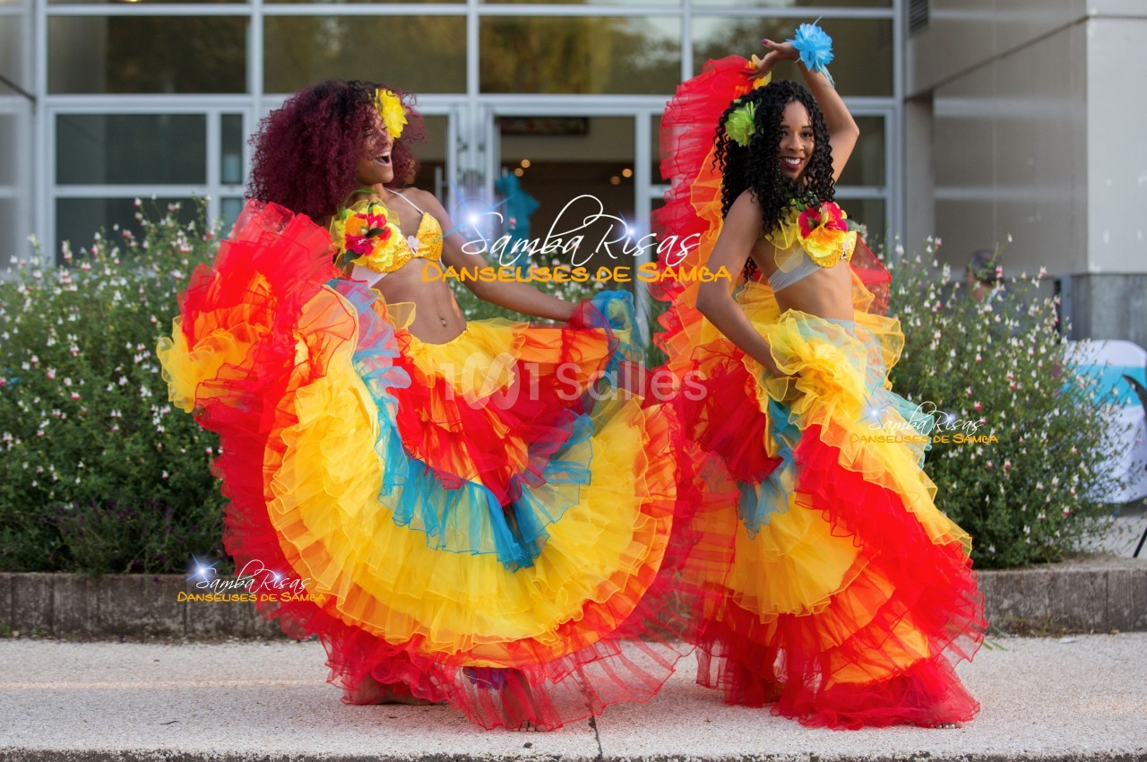 Deux danseuses en tenue colorée de samba exécutent une performance devant un bâtiment moderne.