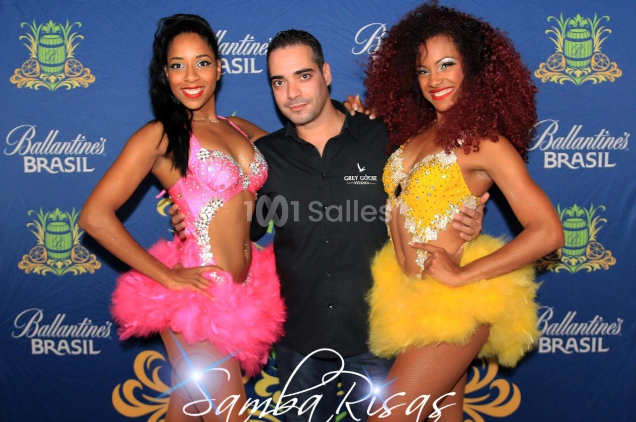 Deux danseuses en tenues colorées posent avec un homme devant un fond promotionnel.