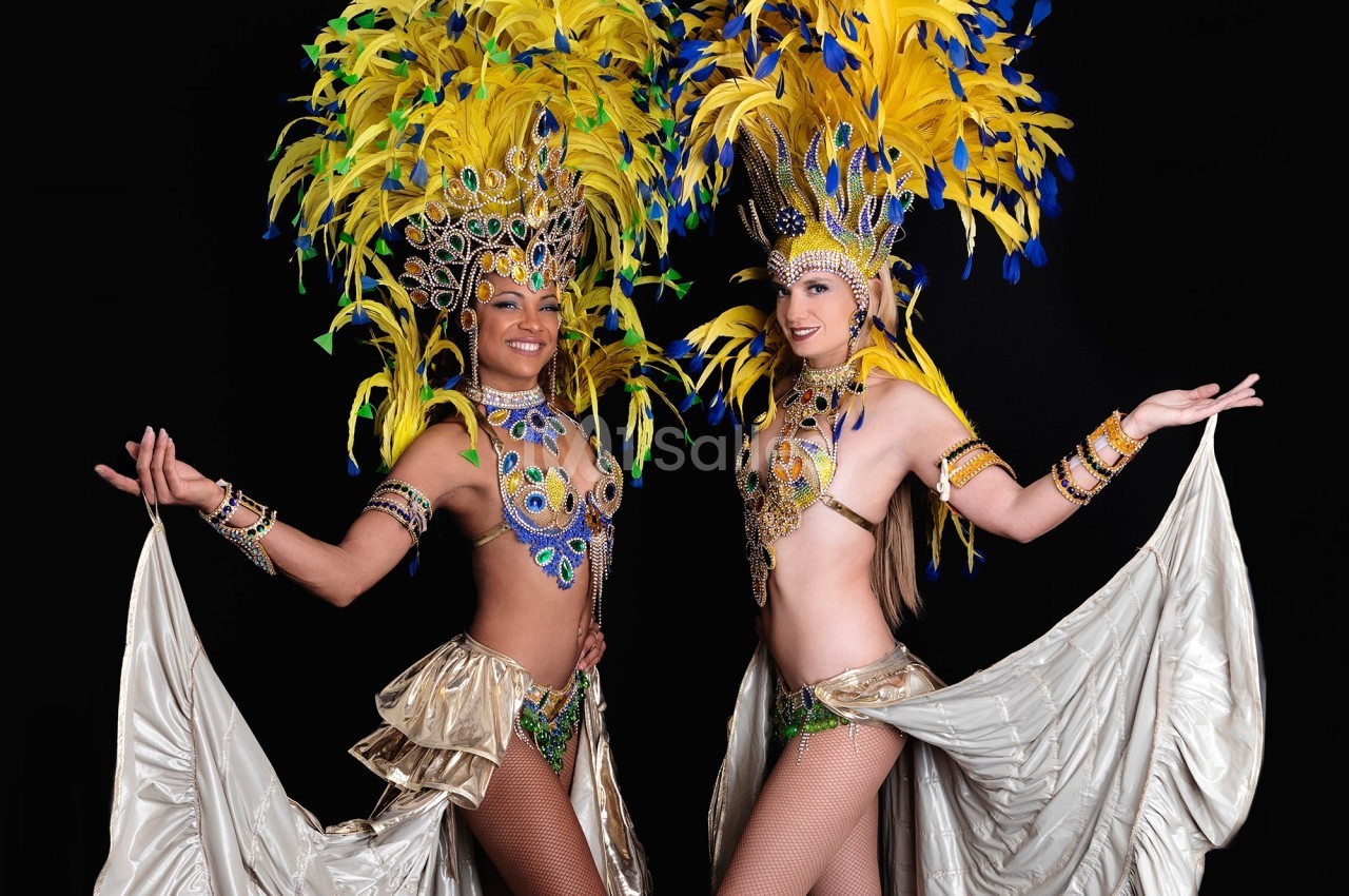Deux danseuses en costumes colorés avec plumes jaunes et bleues, posant sur un fond noir.
