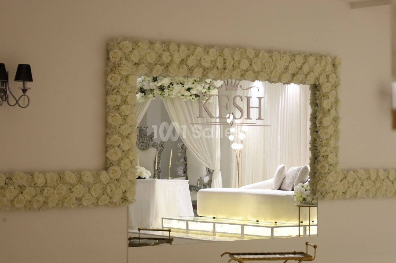 Grand miroir encadré de roses blanches reflétant un salon élégant avec canapé clair et décorations lumineuses.