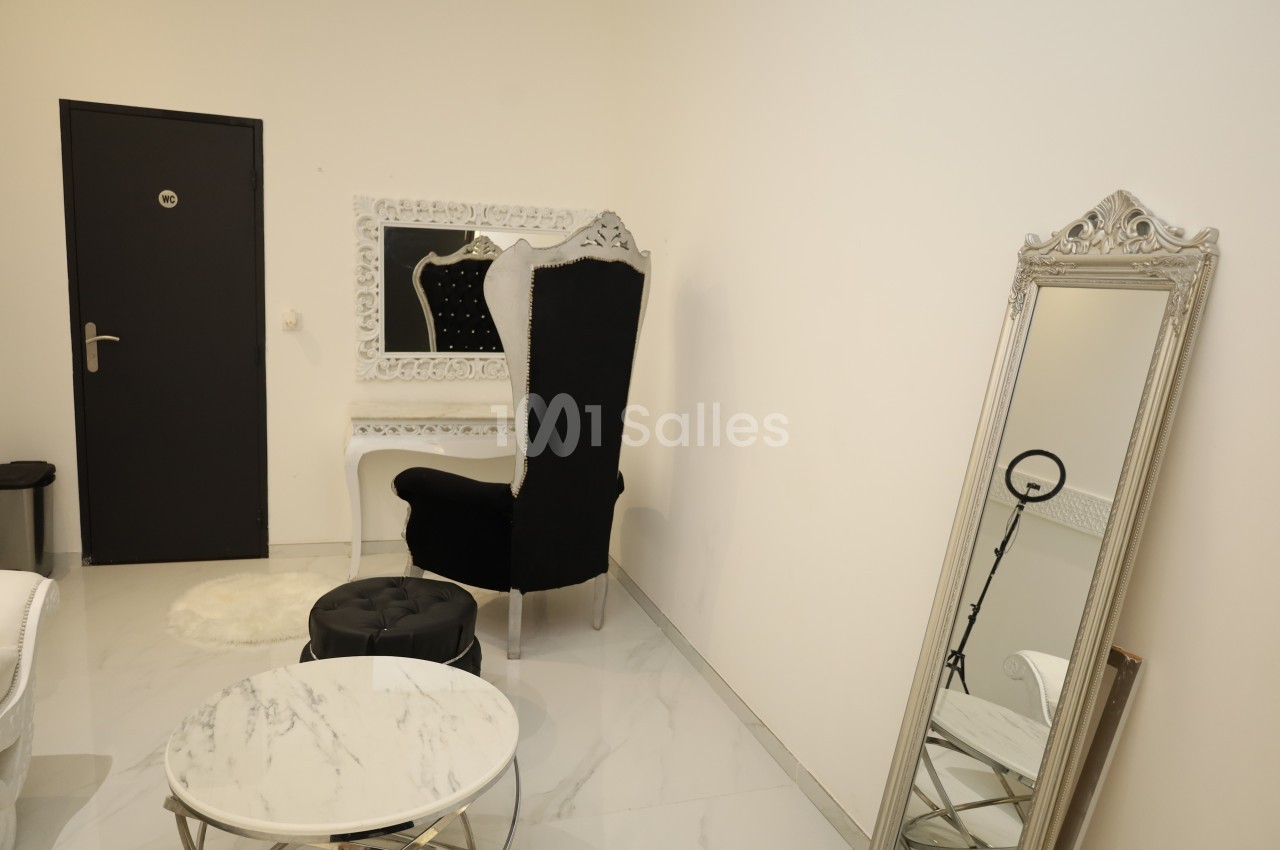 Salle lumineuse avec fauteuil noir, coiffeuse blanche, miroir sur pied et table basse ronde en marbre.