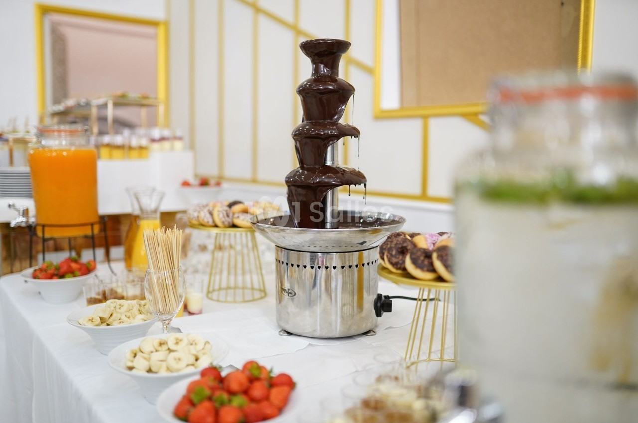 Fontaine à chocolat entourée de fruits frais, brochettes et pâtisseries sur une table de buffet.