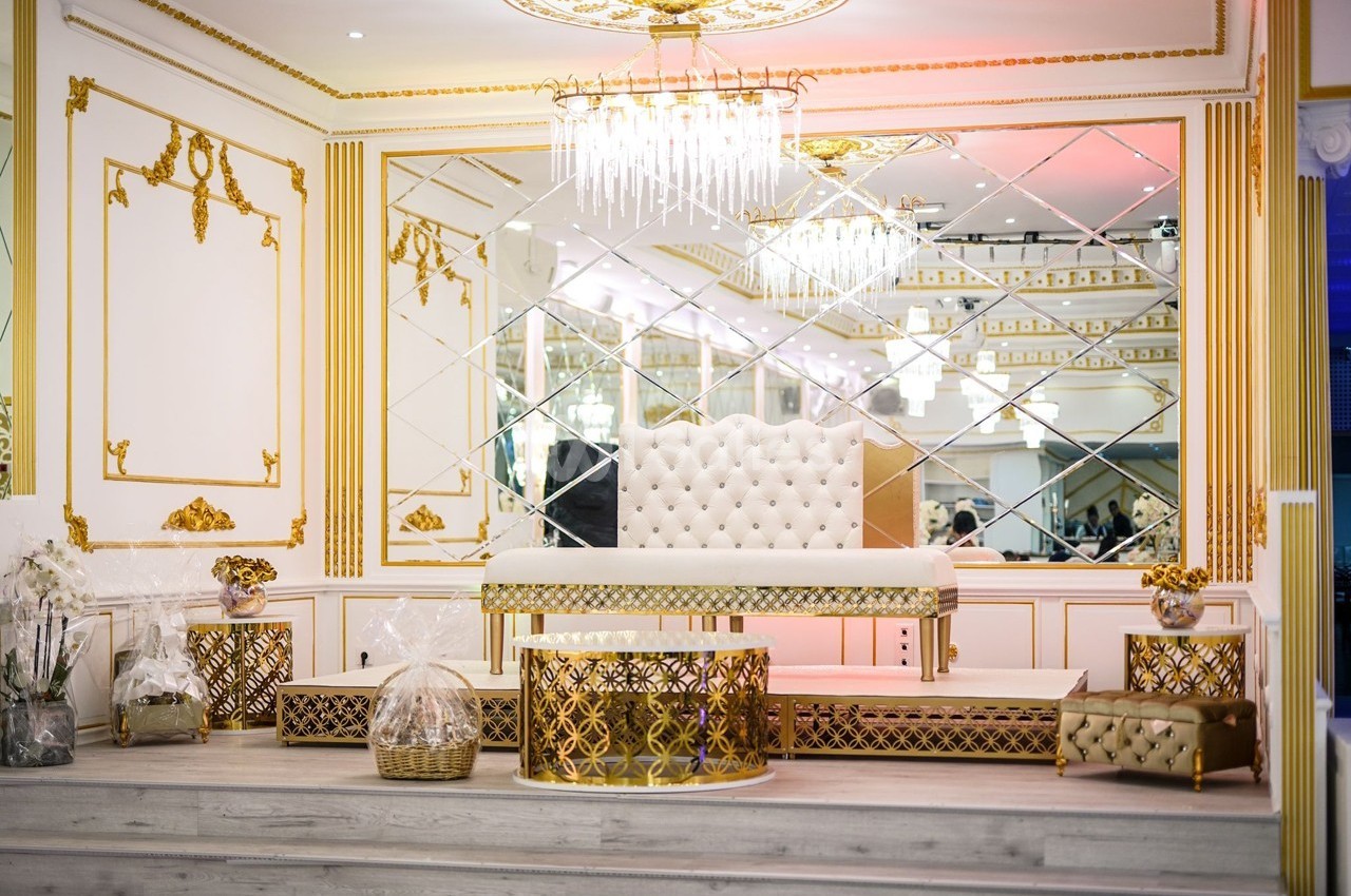 Salle de réception luxueuse avec décor doré, banquette capitonnée blanche et miroirs muraux réfléchissants.