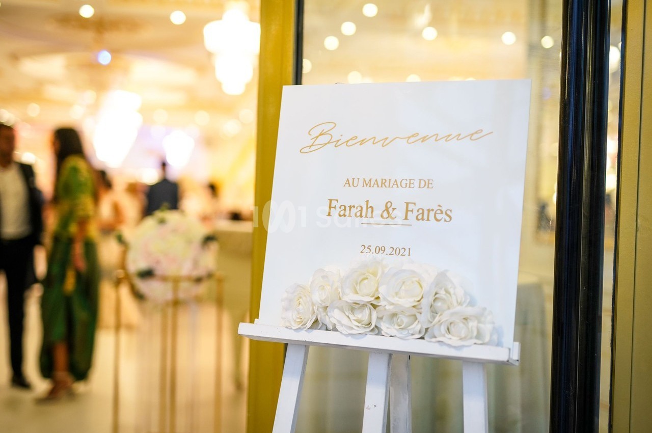 Panneau de bienvenue au mariage de Farah et Farès, décoré de roses blanches, posé sur un chevalet.