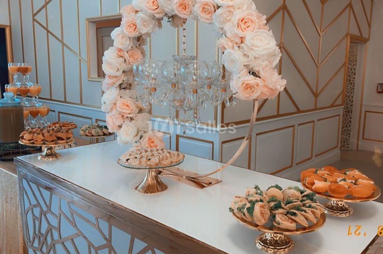 Table décorée avec des fleurs et un lustre, présentant des plateaux de pâtisseries variées dans un cadre élégant.