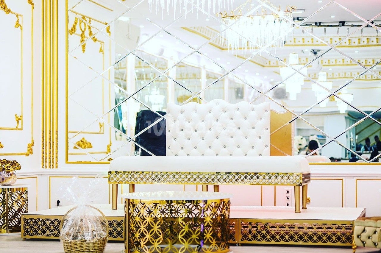 Salle décorée avec des motifs dorés, un banc capitonné blanc et des miroirs en arrière-plan.