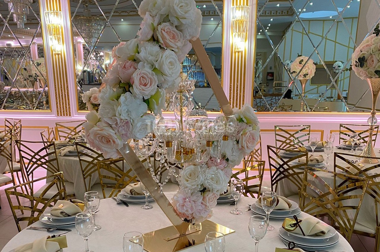 Centre de table floral avec roses blanches et roses, disposé autour d'un chandelier doré sur une table élégamment dressée.