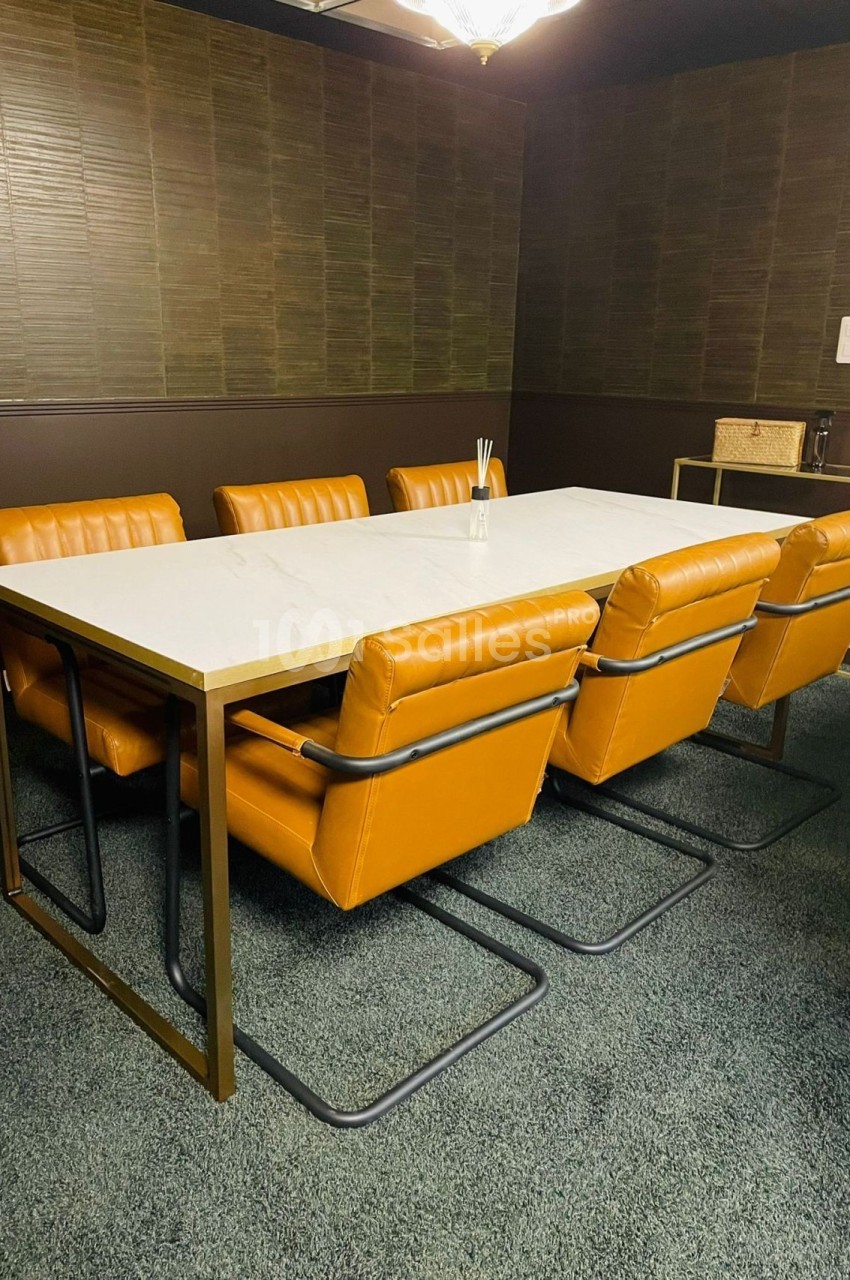 Salle de réunion avec table blanche, six chaises en cuir orange et mur en bois sombre.